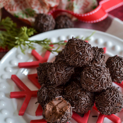 A pile of chocolate rum balls on a white plate with a red snowflake underneath.