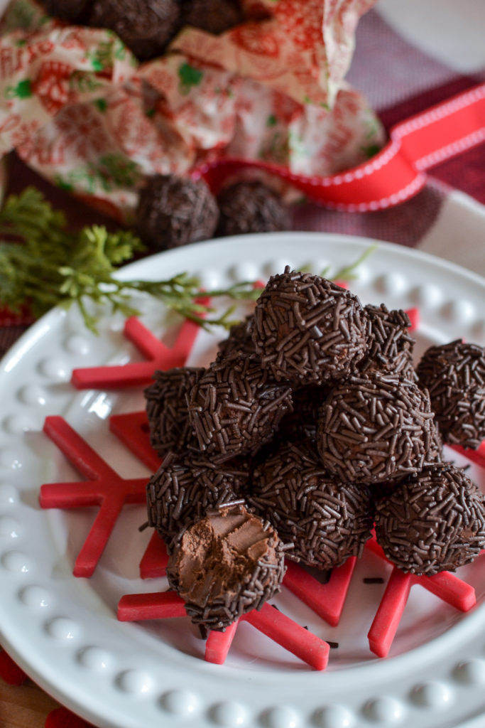 A pile of chocolate rum balls on a white plate with a red snowflake underneath.