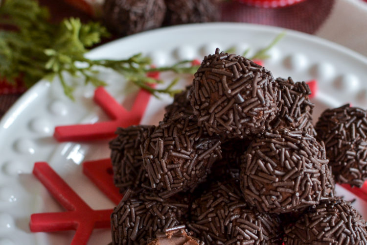 A pile of chocolate rum balls on a white plate with a red snowflake underneath.
