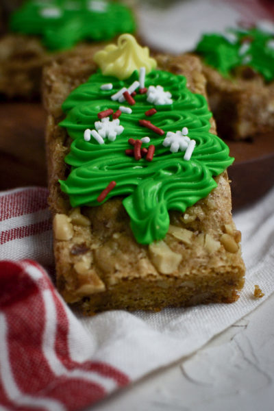 A close up of a blondie cookie bar decorated with a green frosted Christmas tree and sprinkles.