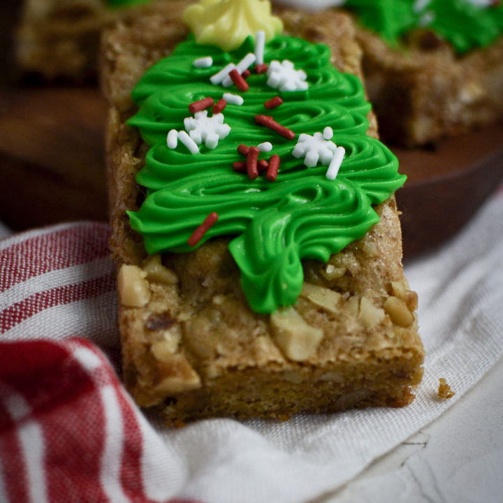 A close up of a blondie cookie bar decorated with a green frosted Christmas tree and sprinkles.