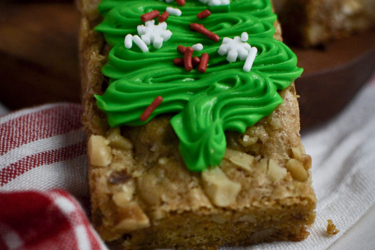 A close up of a blondie cookie bar decorated with a green frosted Christmas tree and sprinkles.