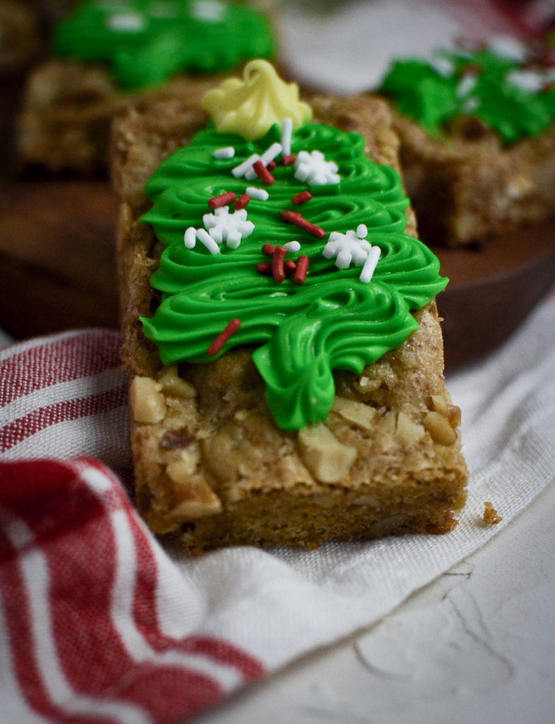 A close up of a blondie cookie bar decorated with a green frosted Christmas tree and sprinkles.