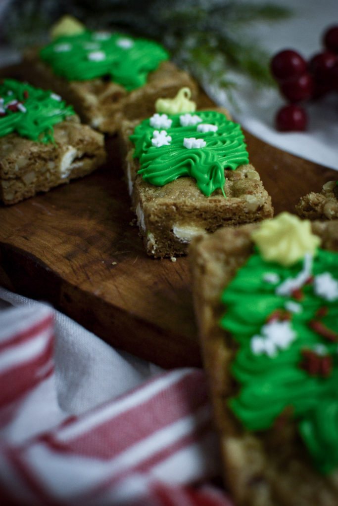 A close up view of chewy christmas blondie bars decorated with green frosting Christmas trees.