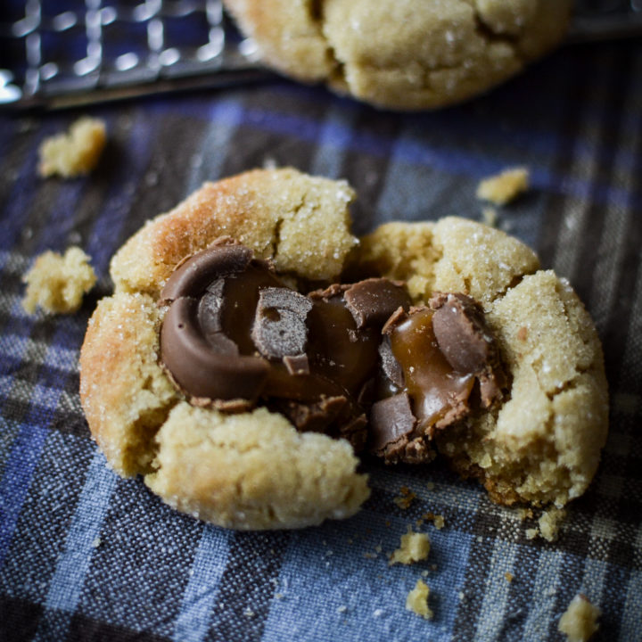 A close up of a chocolate caramel cookie that has been pulled apart to show the gooey caramel.