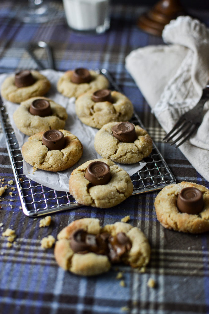 A cooling rack with freshly baked chocolate caramel peanut butter thumbprint cookies.