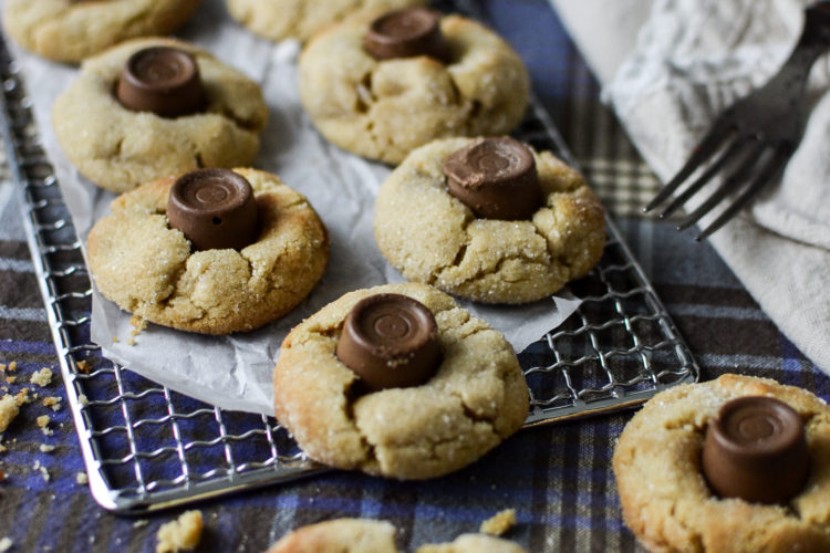 A cooling rack with freshly baked chocolate caramel peanut butter thumbprint cookies.