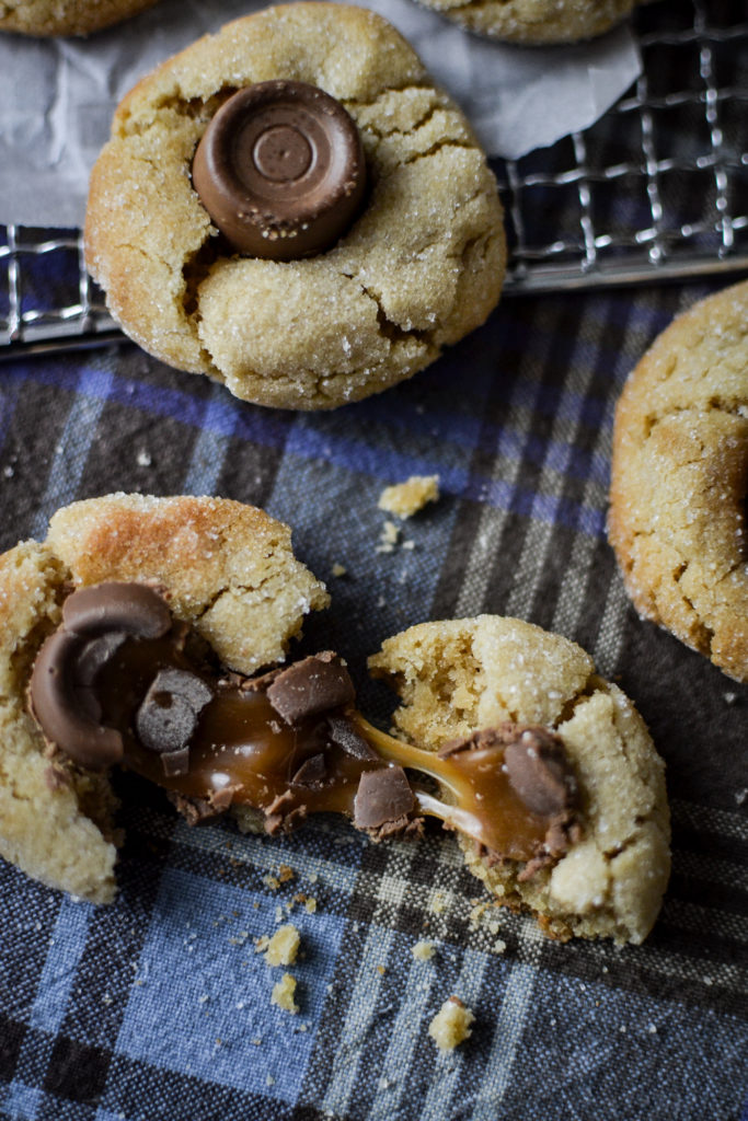 A peanut butter chocolate thumbprint cookie pulled apart stretching the gooey caramel and chocolate.