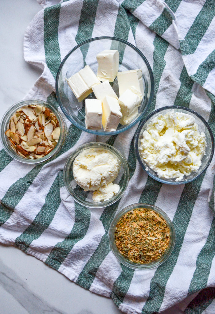 Cream cheese, goats cheese, ricotta cheese, slices almonds and onion chive dip mix in little bowls on a green striped dish towel
