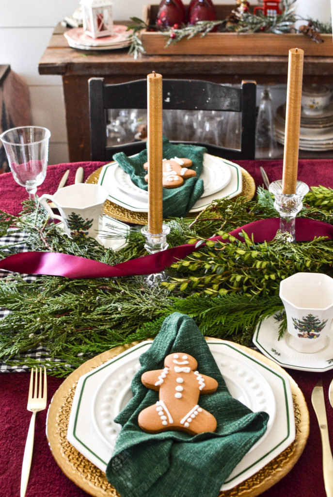 Cranberry ribbon runs along fresh greenery arranged down the centre of a Christmas table.