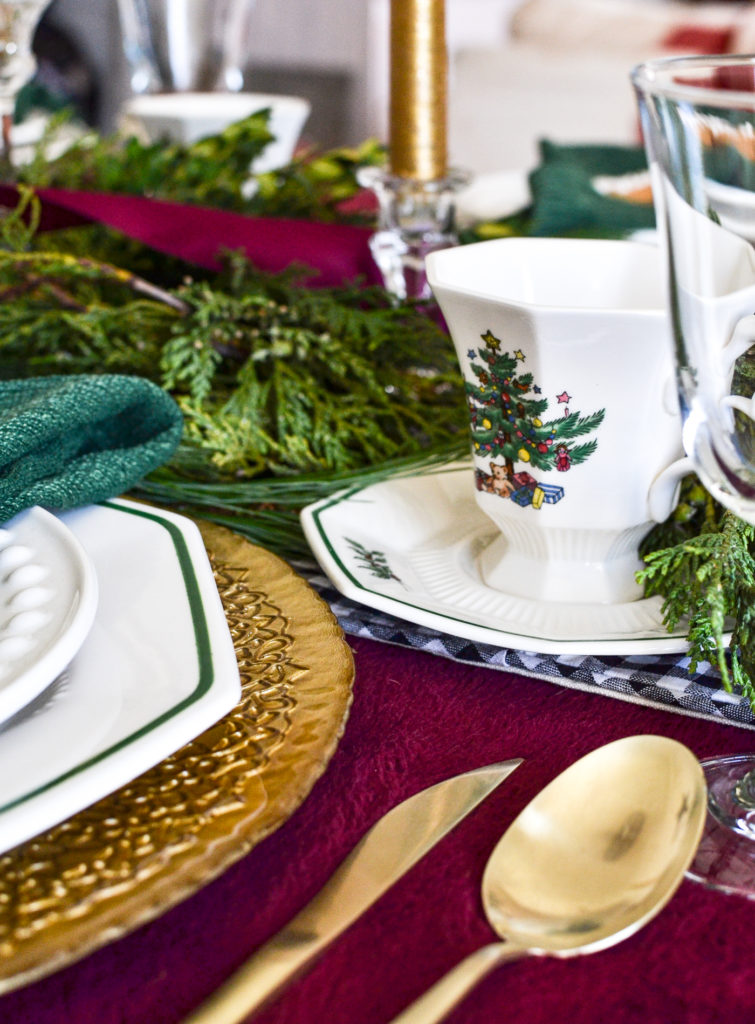 A small view of a plate stack on a table style for Christmas with gold flatware, china teacup and gold charge plate under white dinner and salad plates