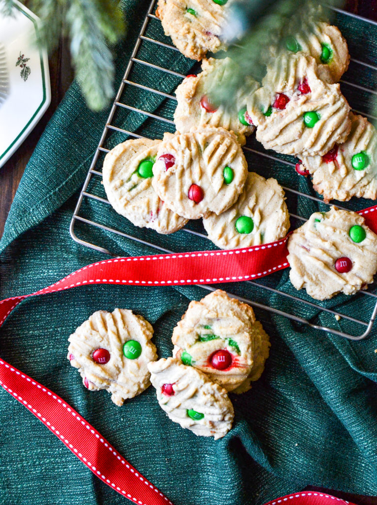 An overhead view of Peanut Butter m&m cookies on a green linen napkin with red ribbon.