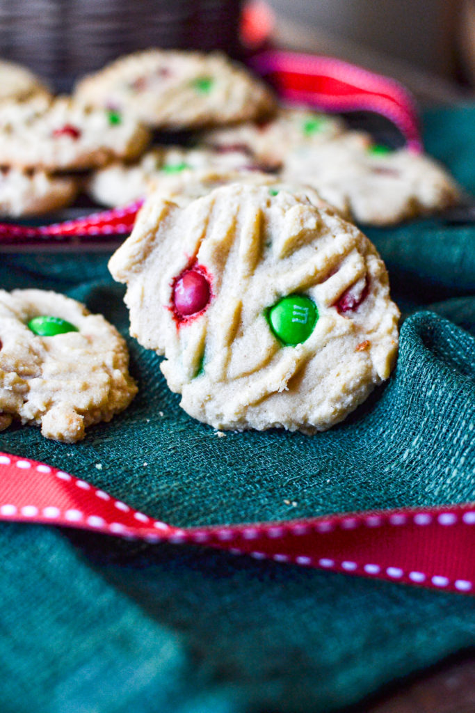 A straight on view of a peanut butter cookie dotted with green and red m&m chocolate candies