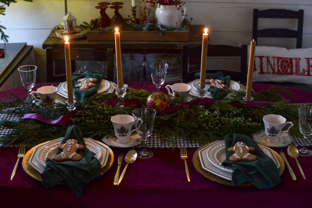 A Christmas tablescape with gold taper candles lit, casting a glow on the greenery and dinner plates