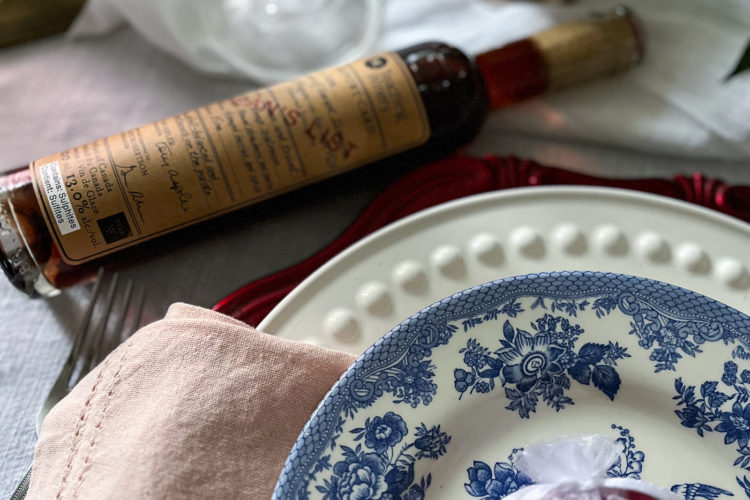 The corner of a plate stack on a valentines tablescape with a bottle of ice wine.