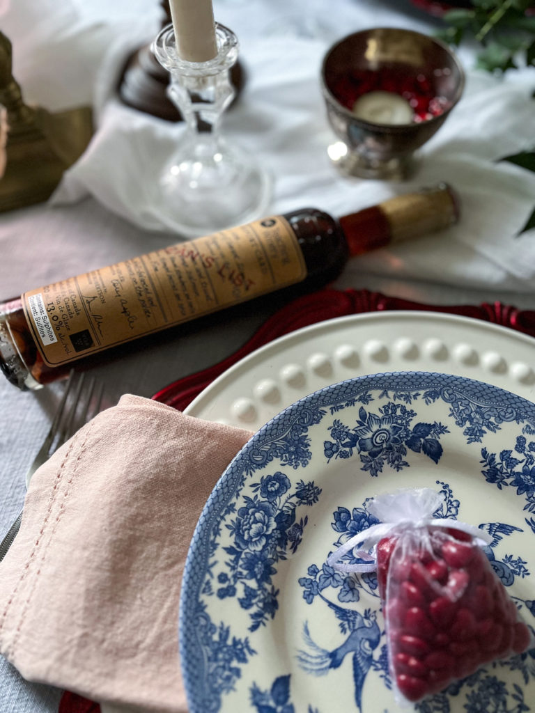 The corner of a plate stack on a valentines tablescape with a bottle of ice wine.