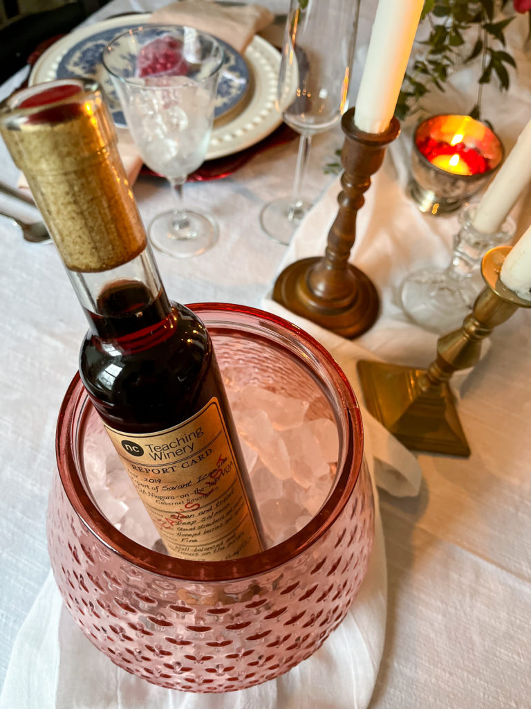 A pink glass vase filled with ice and used as an ice bucket for a bottle of ice wine.