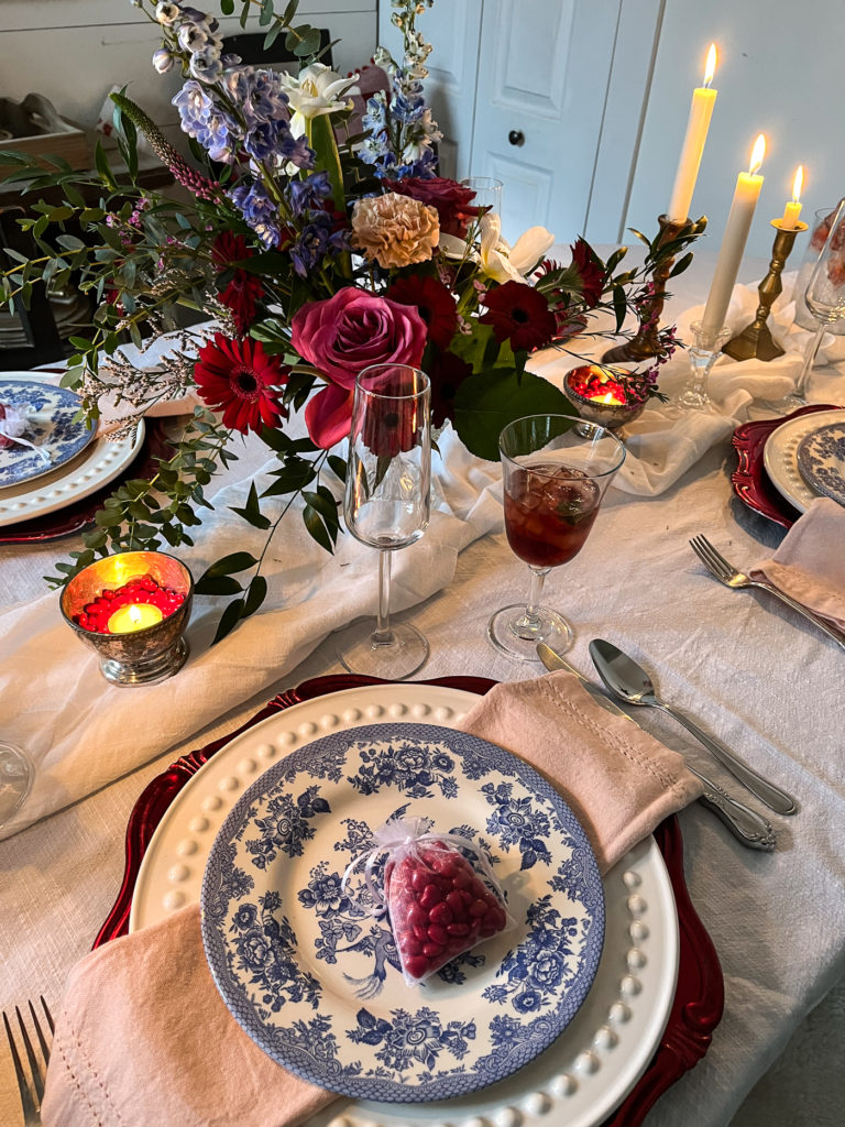 Valentines tablescapes with a bold blue transfer ware plate stack, a floral centrepiece and mismatched wine glasses.