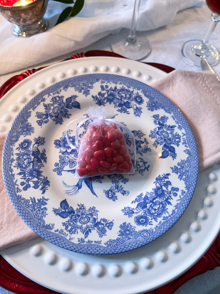 A blue transfer ware plate with a little bag of cinnamon hearts on top.