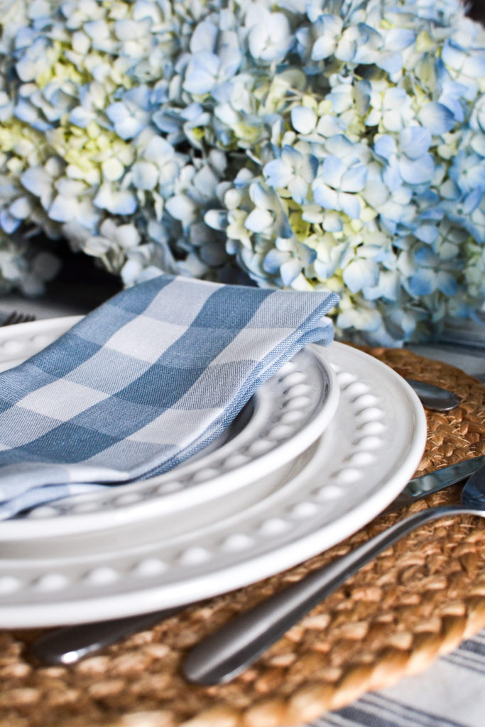 White dinner plates with a beaded edge and a white and blue checked napkin on top.