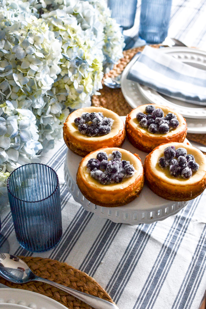 Four cheesecakes topped with sugared blueberries.