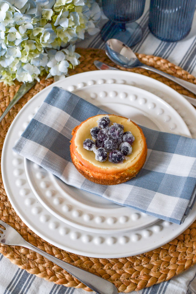 Blueberry topped cheesecake on top of white plates and a blue and white checked napkin.