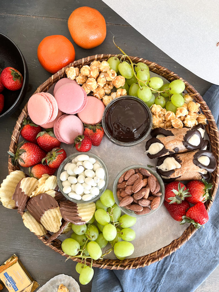 Dessert grazing board almost full with grapes, strawberries, cookies, chocolate dipped potato chips.