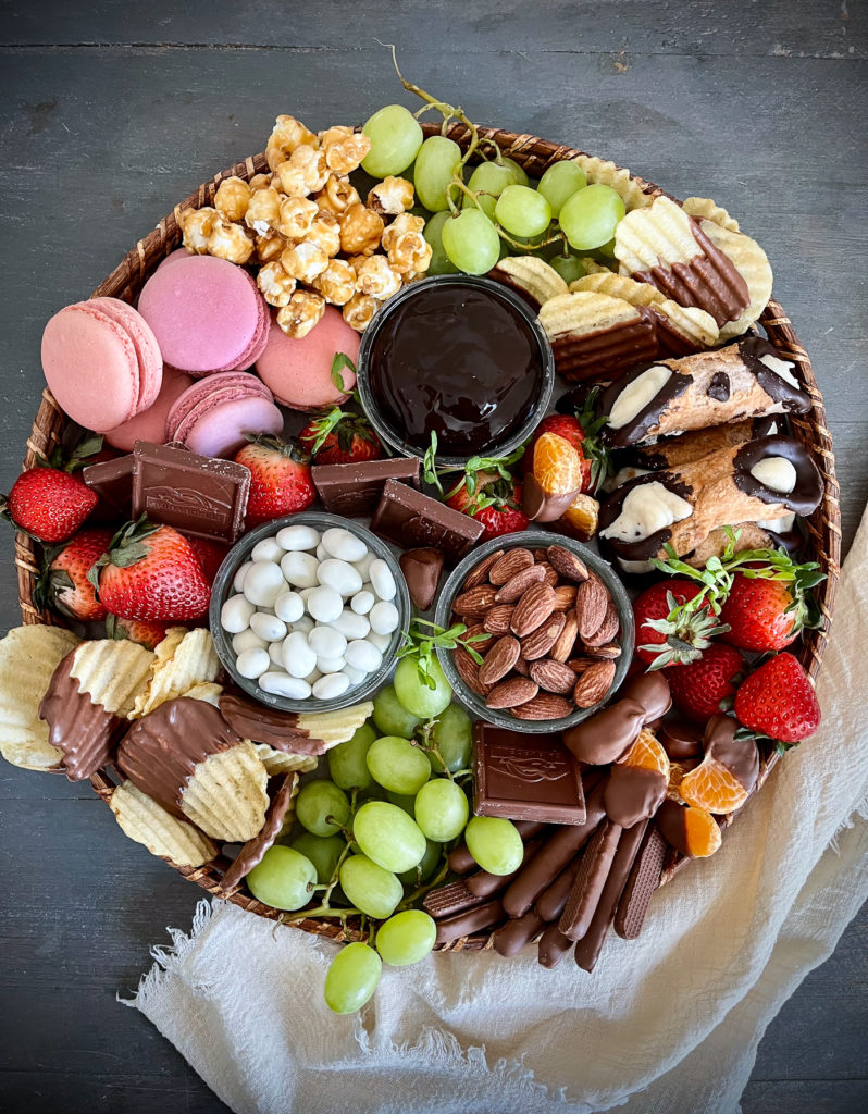 An overhead view of a dessert charcuterie board with nuts, cookies, cannolis, grapes, strawberries, and chocolate dipped potato chips