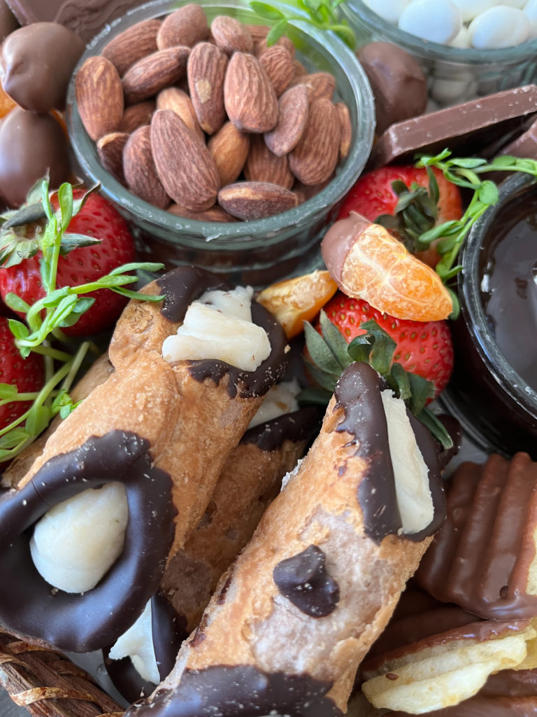 Close up of the cannoli, strawberries, and chocolate dipped oranges on a dessert grazing board