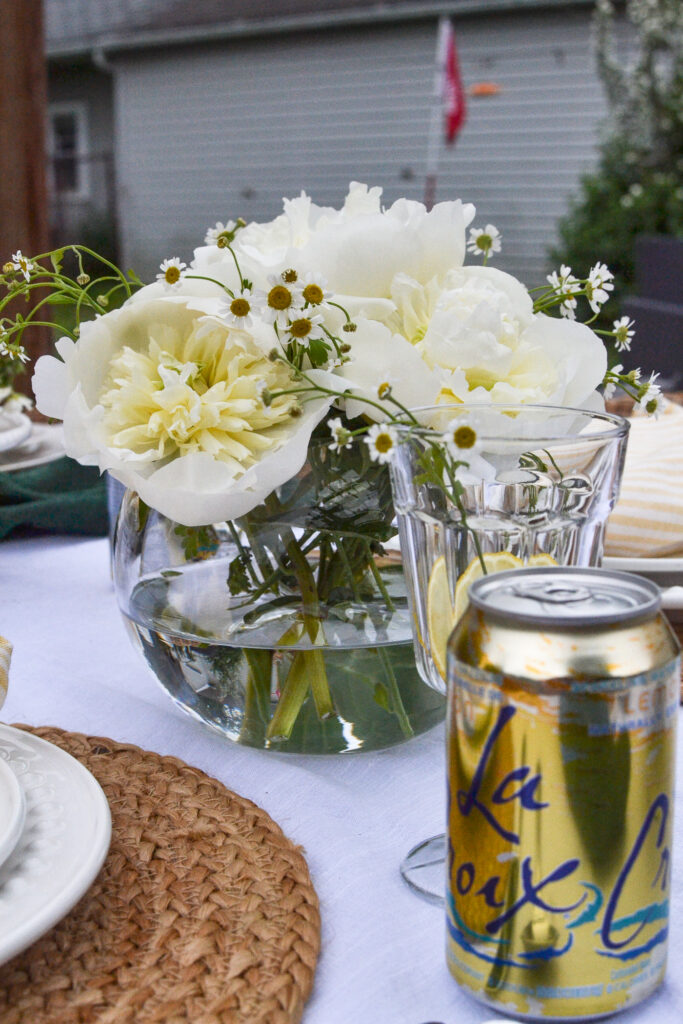 White peonies arranged in a rose bowl.  A can of lemon La Croix water in the forground.