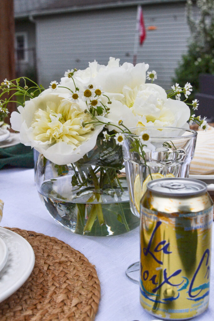 White peonies arranged in a rose bowl. A can of lemon La Croix water in the forground.