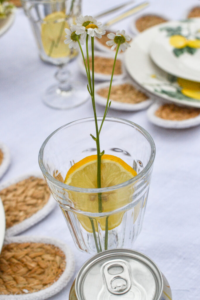 A glass with a slice of lemon and a sprig of organic chamomile.