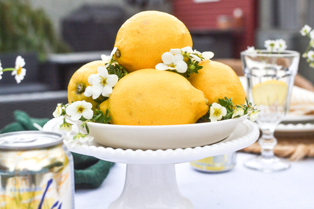 An arrangement of lemons and tiny white blossoms arranged on top of a cake plate.