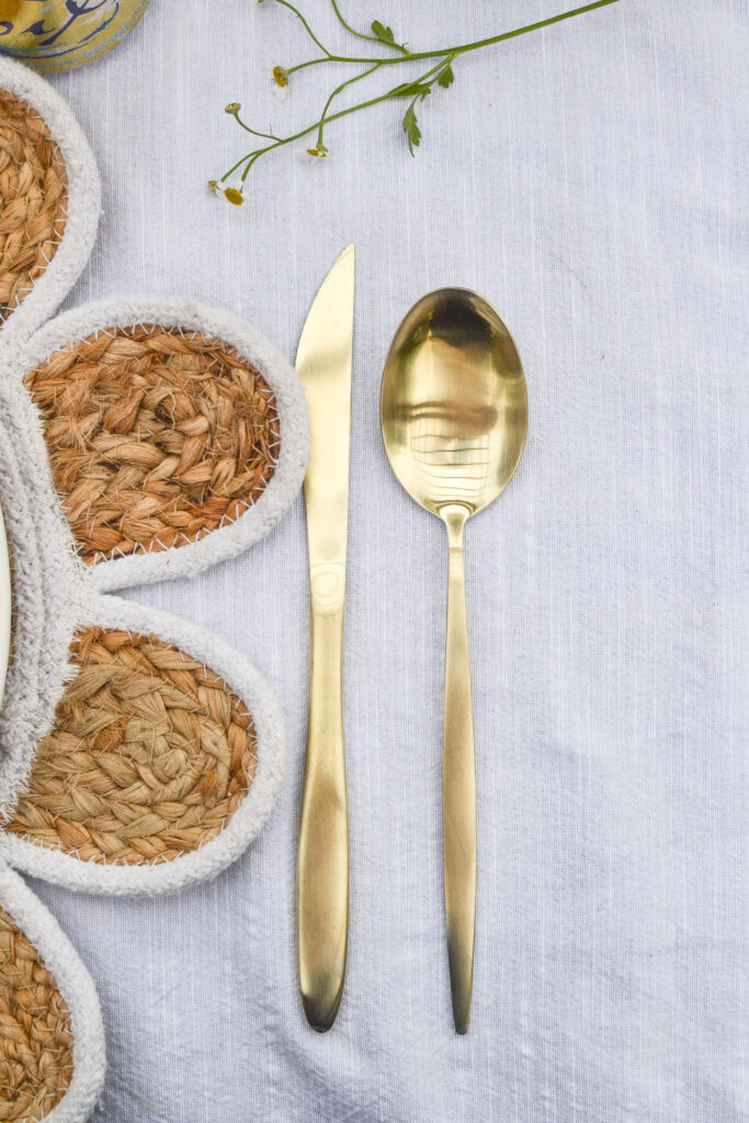 Gold knife and spoon sit alongside a glimpse of a daisy shaped place mat, with a sprig of camomile.