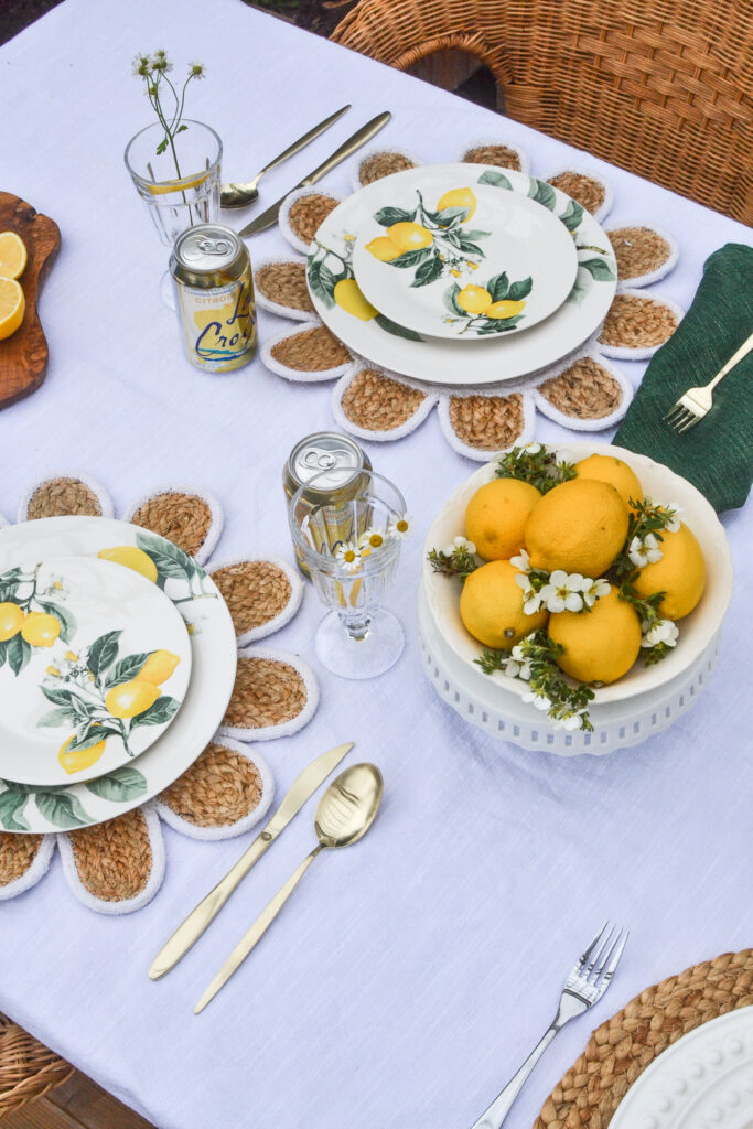 Lemon themed dinner plates on top of a white tablecloth with a centrepiece of fresh lemons.