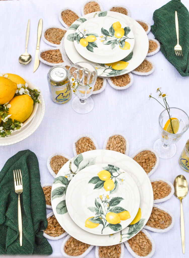 Lemon themed dinner plates on top of daisy shaped rattan place mats, with green napkins and gold flatware.