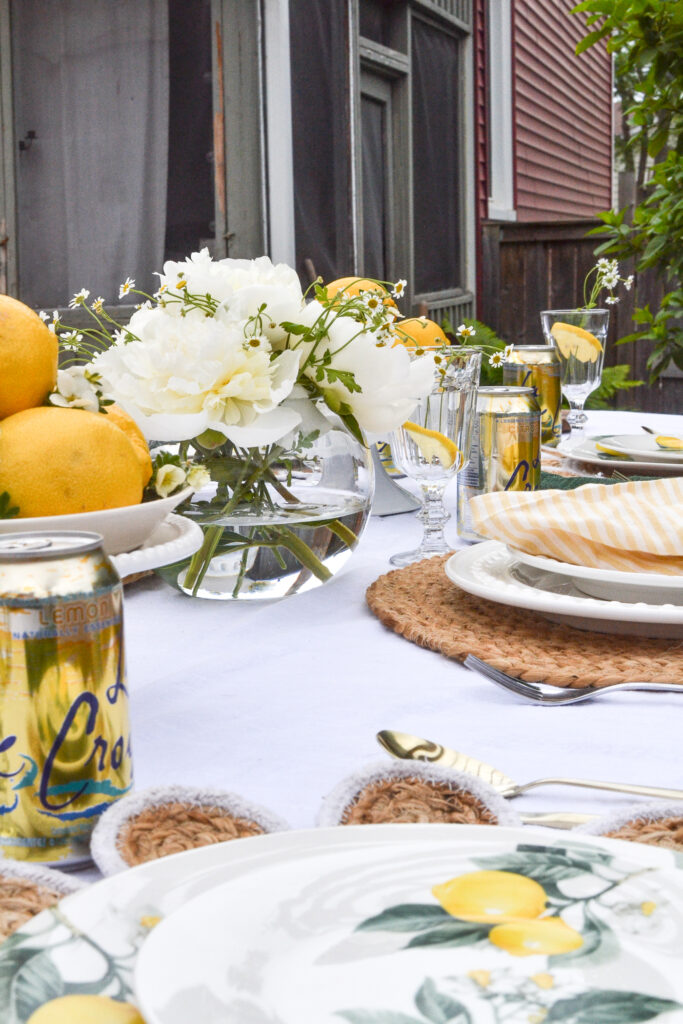 An outdoor table set with lemon themed plates, lemon centrepieces and white peony centrepiece.