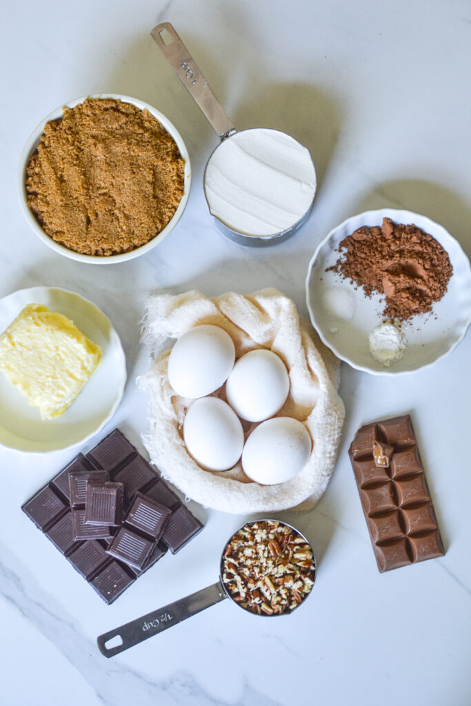 Ingredients to make triple chocolate brownies; eggs, cocoa powder, flour, salt, baking powder, chocolate and pecans