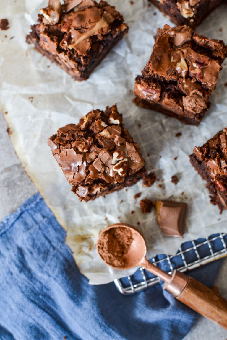 Overhead view of brownies on a cooling rack with a spoonful of cocoa powder beside them.