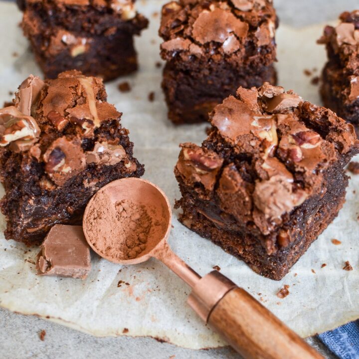 Brownies on top of parchment paper with a spoon full of cocoa powder.