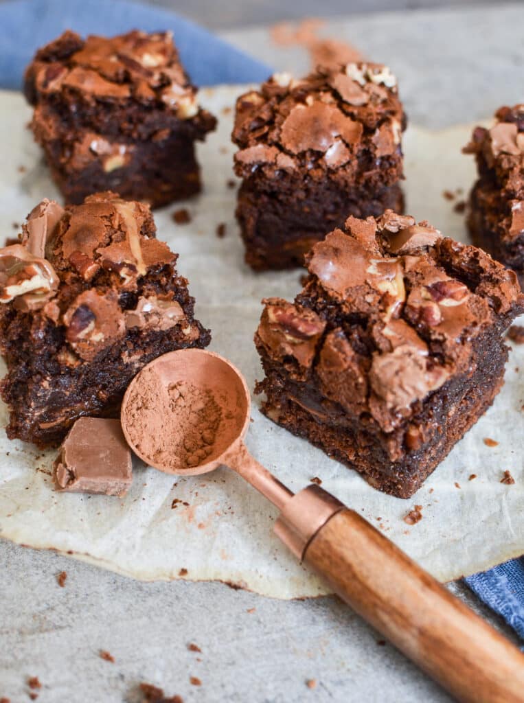 Brownies on top of parchment paper with a spoon full of cocoa powder.