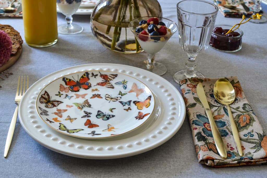 A table set for brunch with butterfly plates, gold flatware and dahlia flowers.