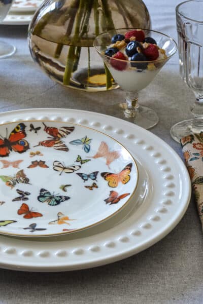 A table set for brunch with butterfly plates, gold flatware and dahlia flowers.