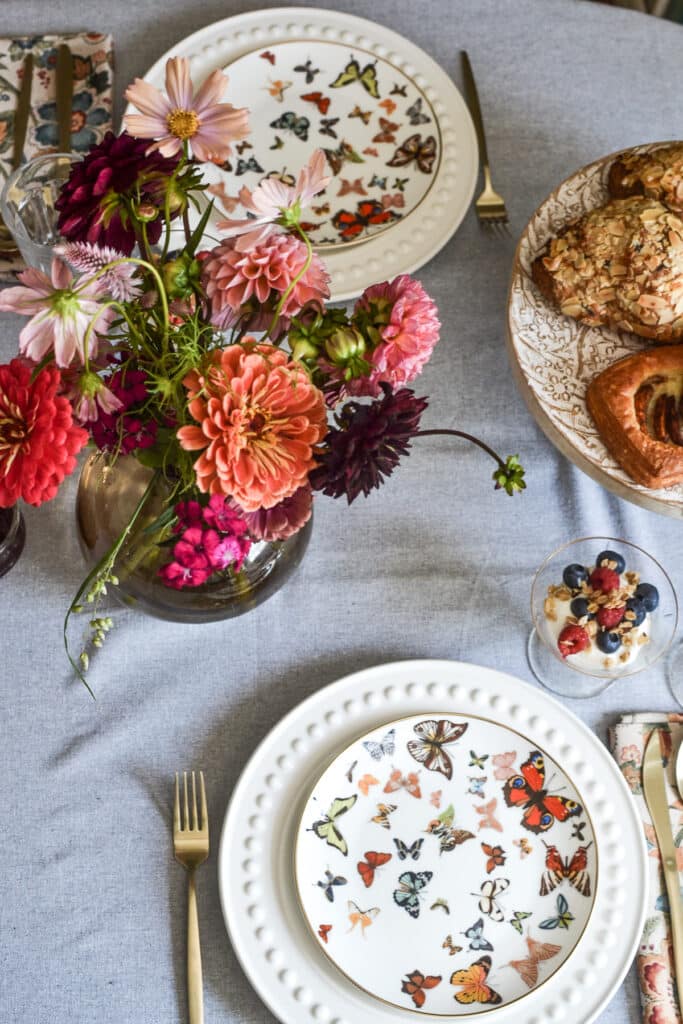 An overhead view of a table set for brunch with butterfly plates, dahlia flowers and a plate of pastries