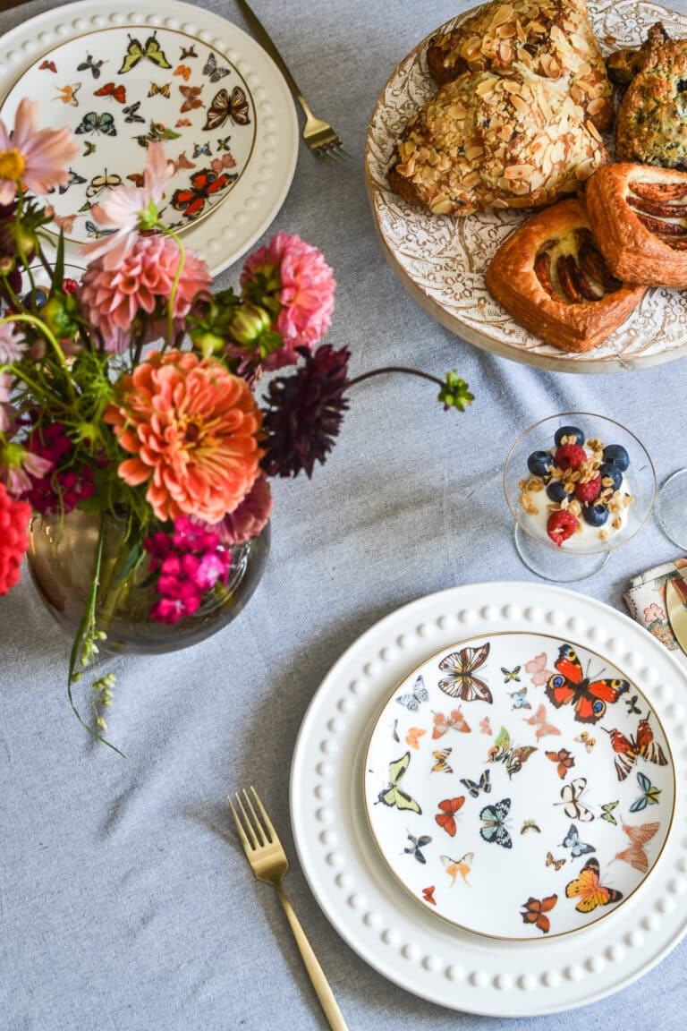 A table set for autumn brunch, with butterfly plates and orange and pink fresh flowers, pastries and yogurt parfait