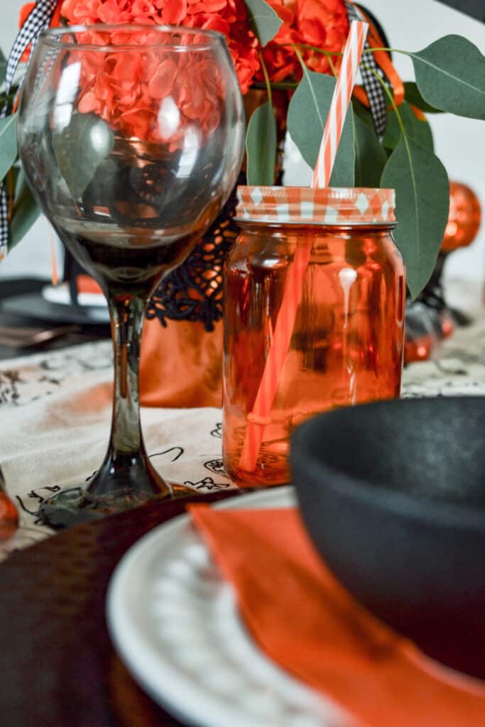 Orange mason jar and black wine glass on a table set for a halloween party.