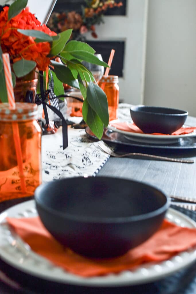 Black bowls and orange jar glasses on a halloween party table.