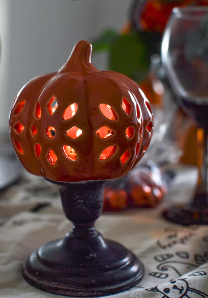 Orange cut-out lighted pumpkin on a black candle stick.