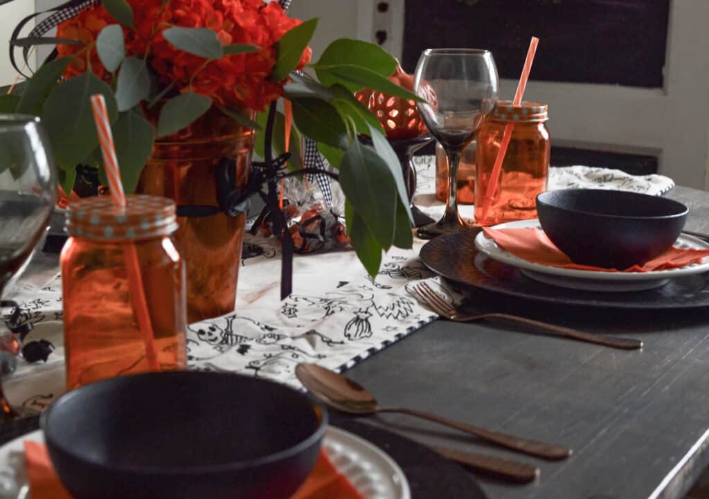 An orange and black tablescape for Halloween showing two place settings and orange hydrangeas.