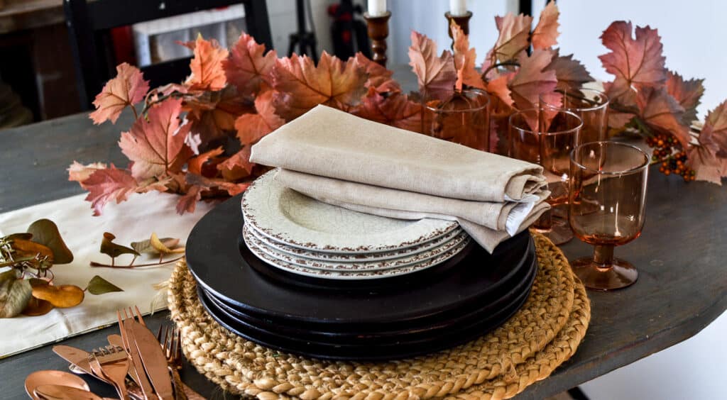 Plates, napkins, glasses and cutlery stacked on a dining room table.